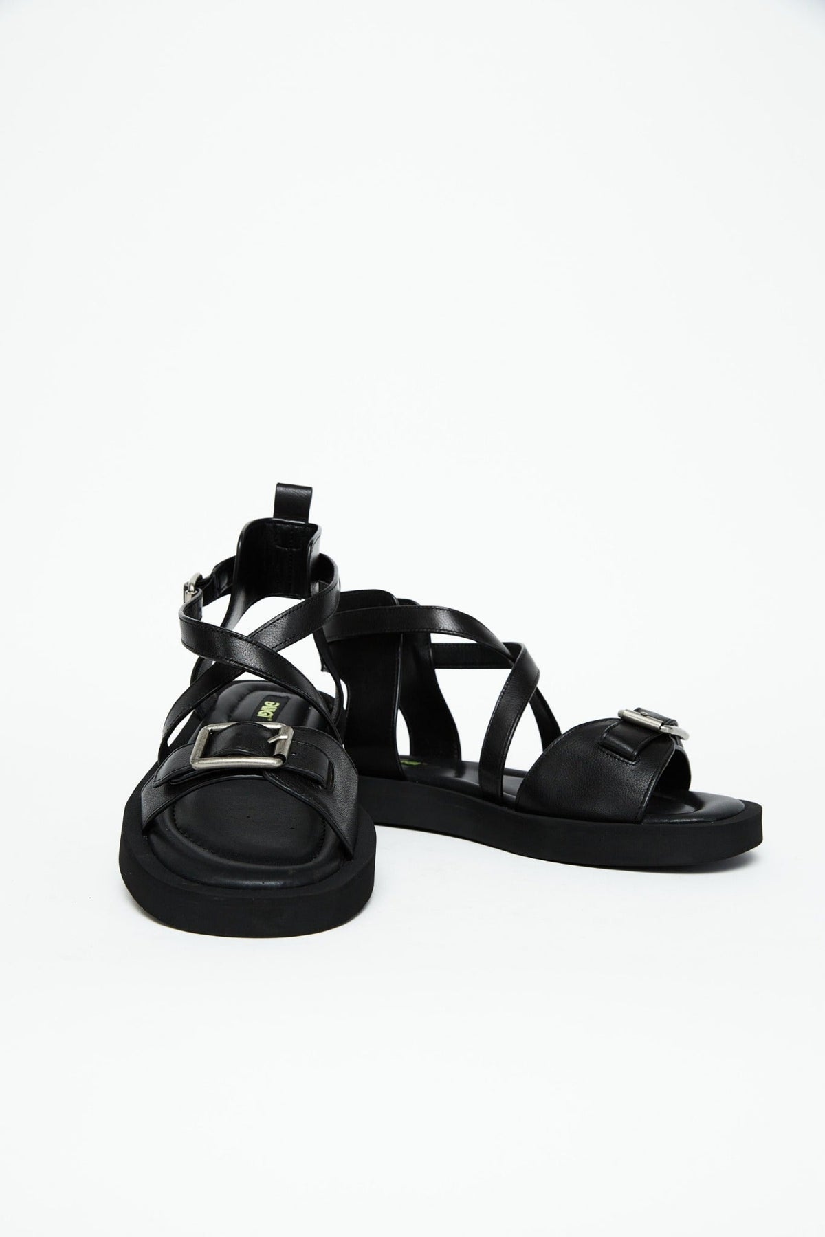 Front view of black leather sandals showing wide buckle straps and crossover construction