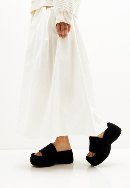 Black textile platform slides styled on a model with an ivory skirt, side view