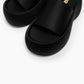 Close-up of black platform slides showing the broad textile strap and footbed