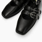 Close-up of black leather ballet flats showing square toes, eyelets and silver buckles
