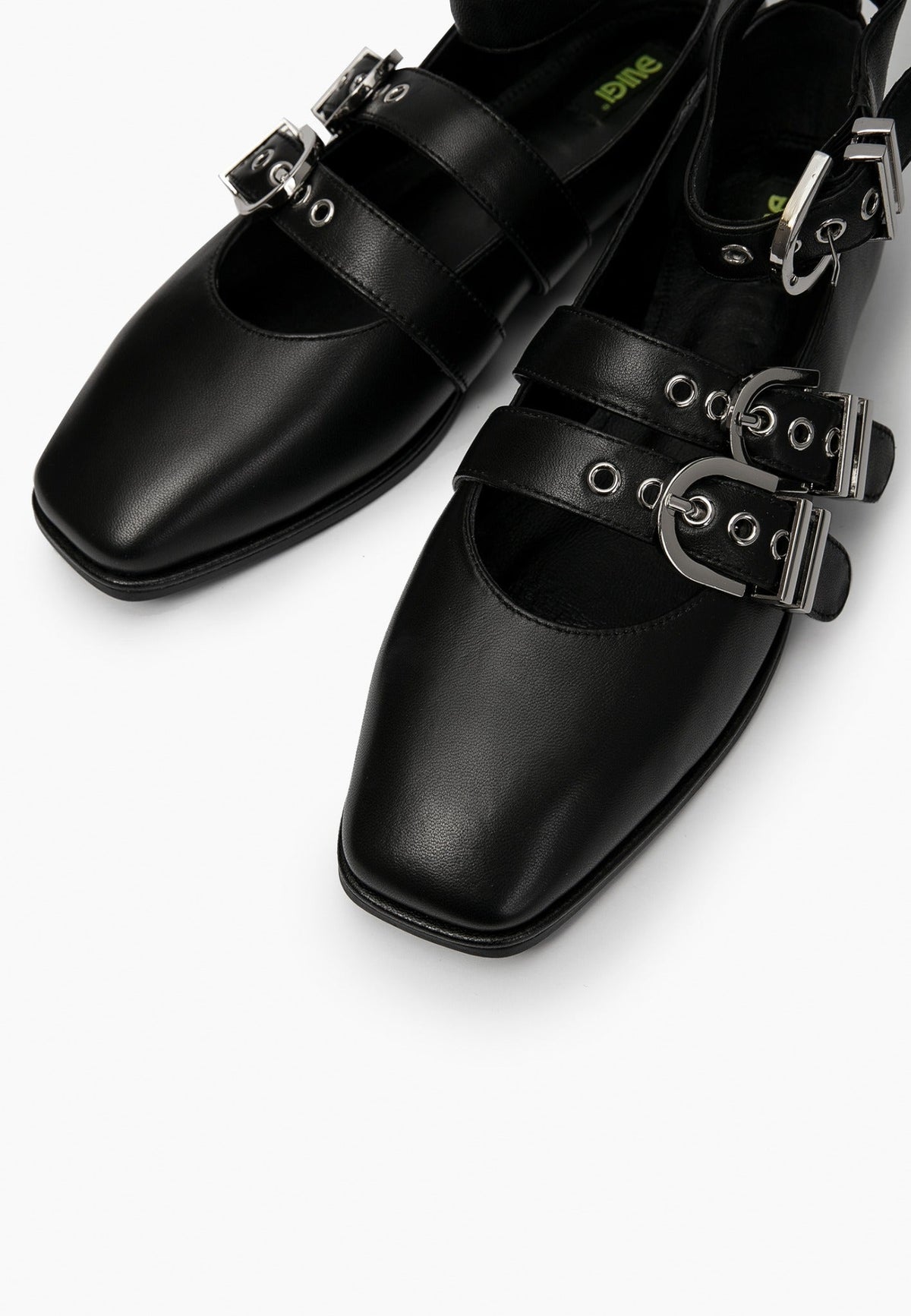 Close-up of black leather ballet flats showing square toes, eyelets and silver buckles