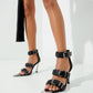 Black leather chrome-detail heels worn on a model, close styling view