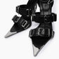 Close-up of wide black leather straps, oversized chrome buckles and pointed toe caps