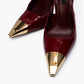 Close-up of glossy burgundy patent leather and sculpted gold-tone toe hardware