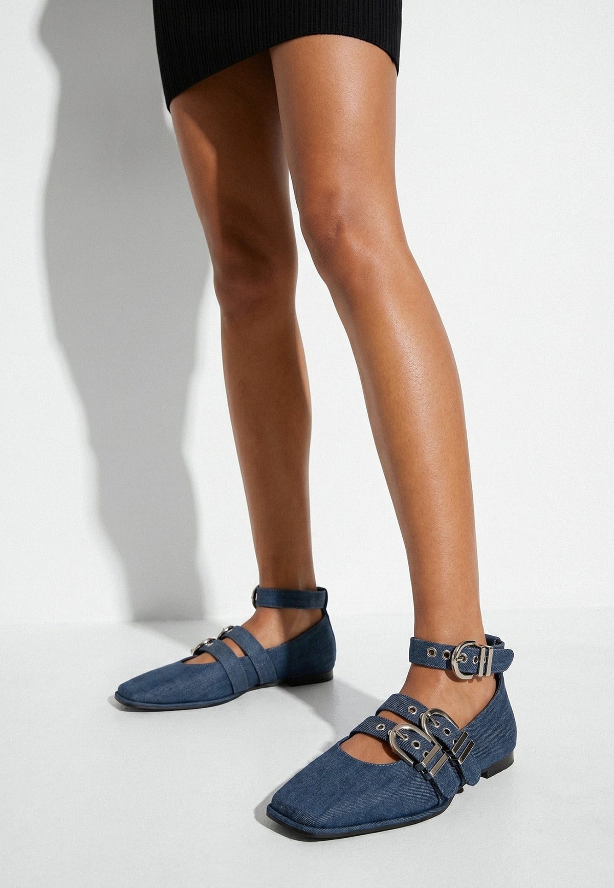 Indigo denim triple-buckle ballet flats worn with a fitted black dress