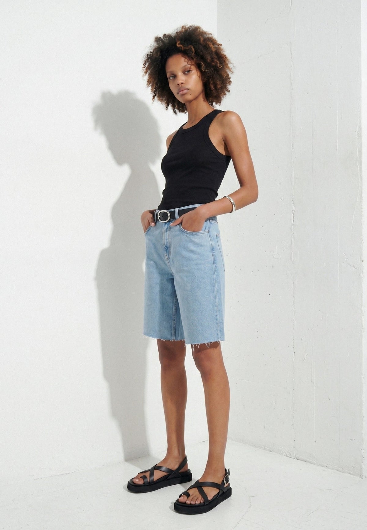 Woman wearing black toe-loop leather flatform sandals with denim shorts in a white studio
