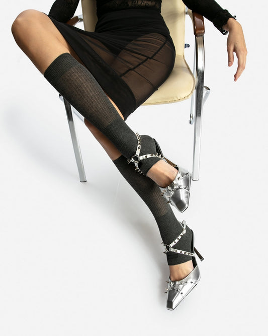 Silver spiked leather heels styled on a seated model with a black skirt and grey knee-high socks