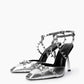 Pair of silver leather heels with heart-shaped rings and crossed spiked straps, three-quarter view
