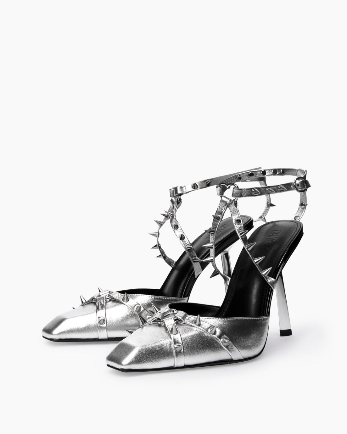 Pair of silver leather heels with heart-shaped rings and crossed spiked straps, three-quarter view