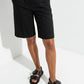 Woman wearing black padded leather sandals with tailored shorts in a white studio